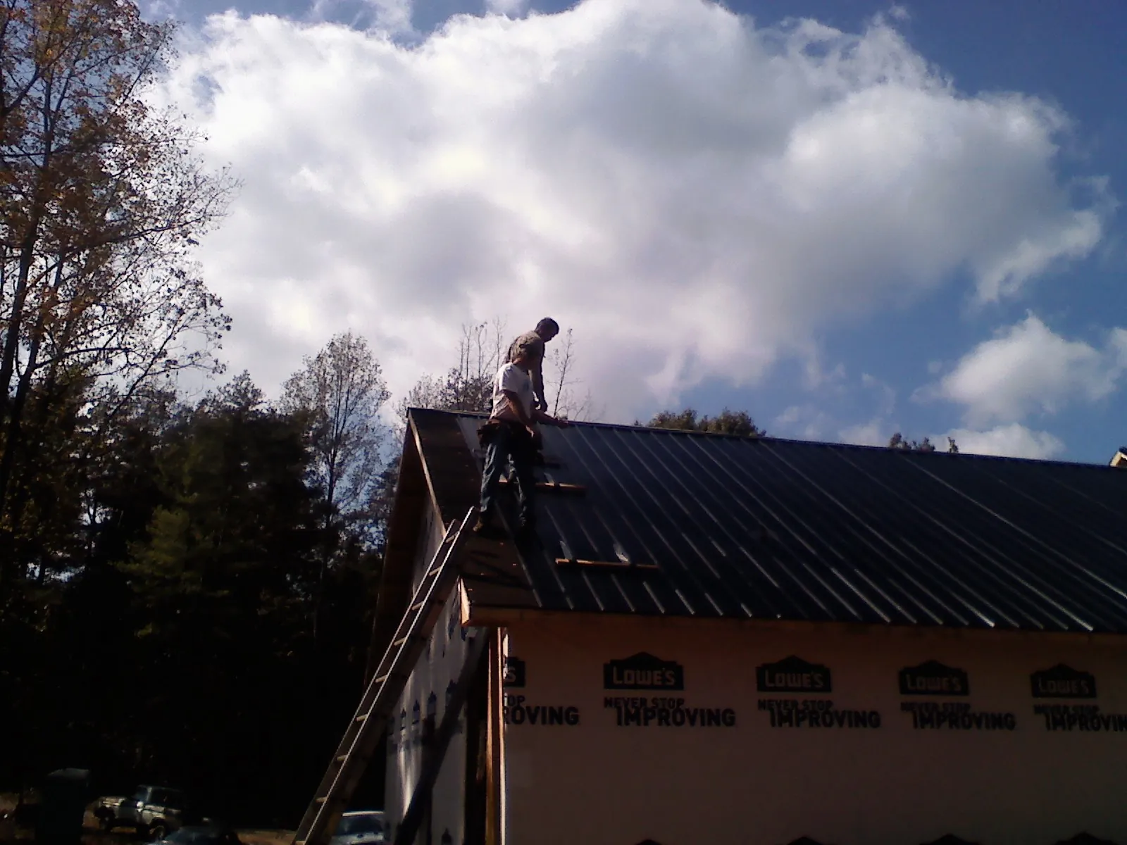Roofer fastening dark metal panels high against a cloudy sky, from a Roof Inspection job in Sanford